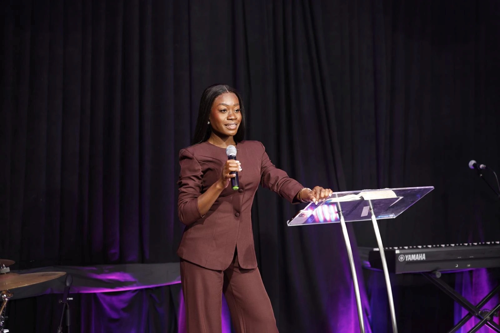 Ink Duncan in a burgundy suit, smiling as she speaks with a microphone at a clear lectern